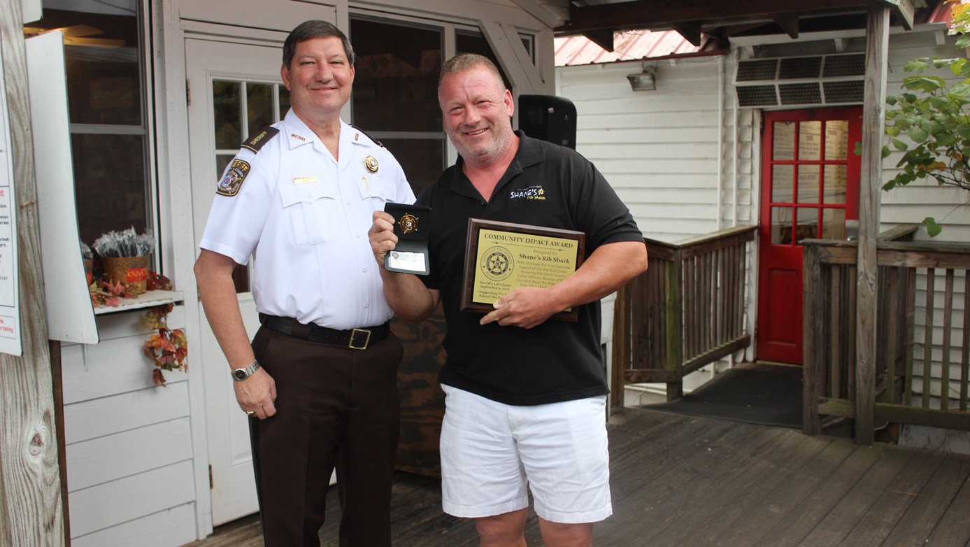 Sheriff Keith McBrayer and Shane Thompson holding the Honorary Deputy Badge and Community Impact Award 