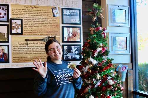 Smiling Shack Crew Employee in front of Christmas Tree with gift card.